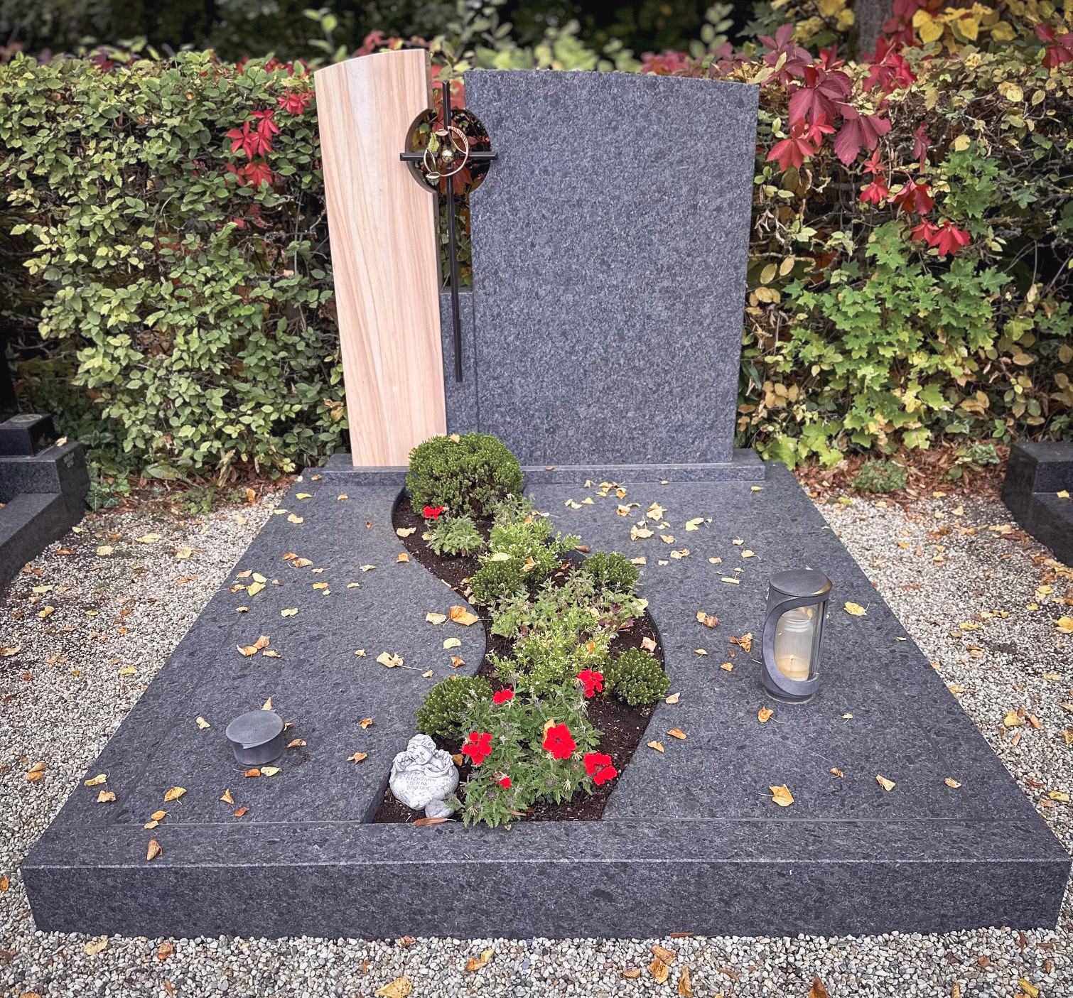 Zweiteiliges Grabmal aus Sandstein und Granit mit bronzenem Kreuz und geschwungener Bepflanzung