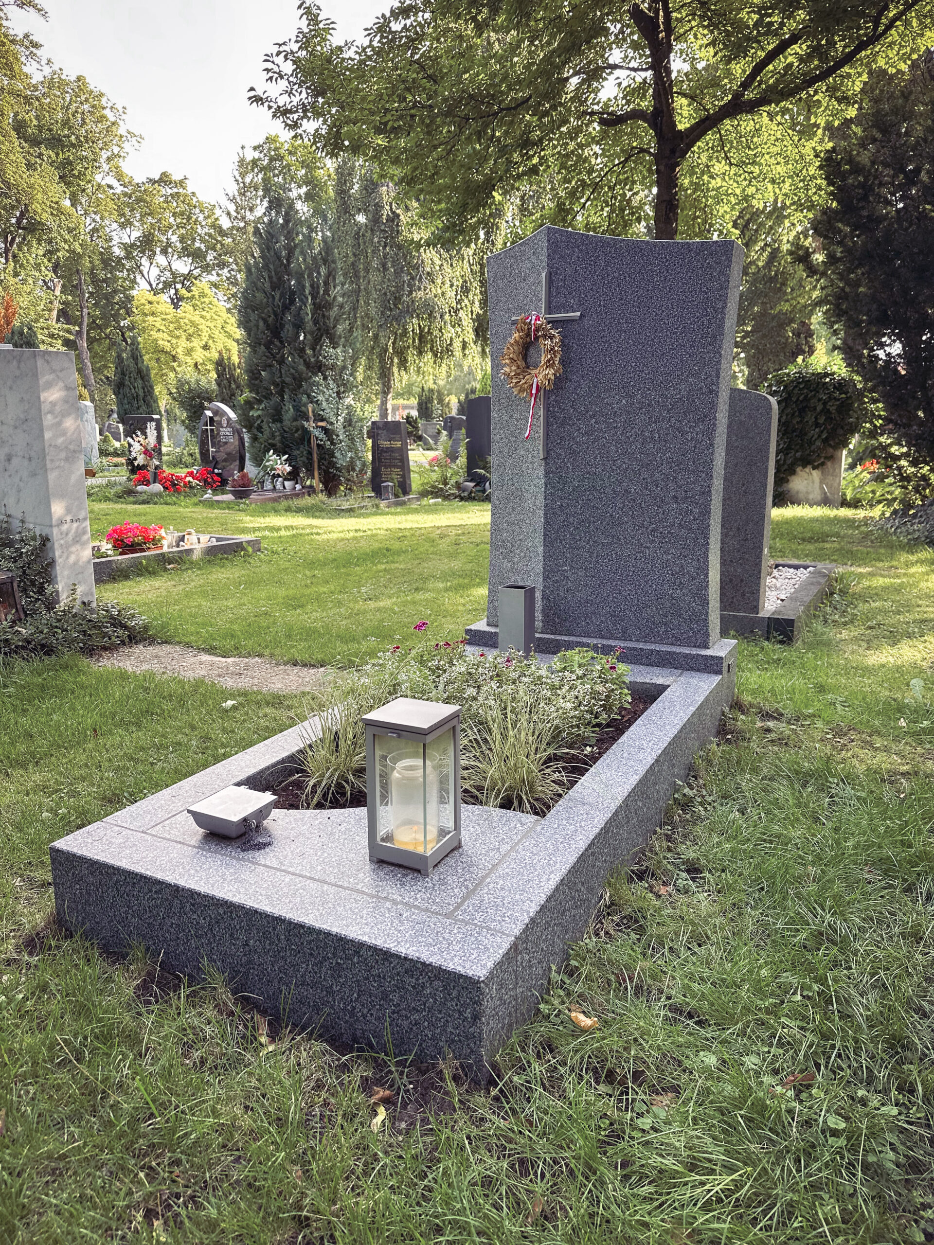 Granit-Grabmal mit bronzenem Kreuz und Trauerkranz im Sommer