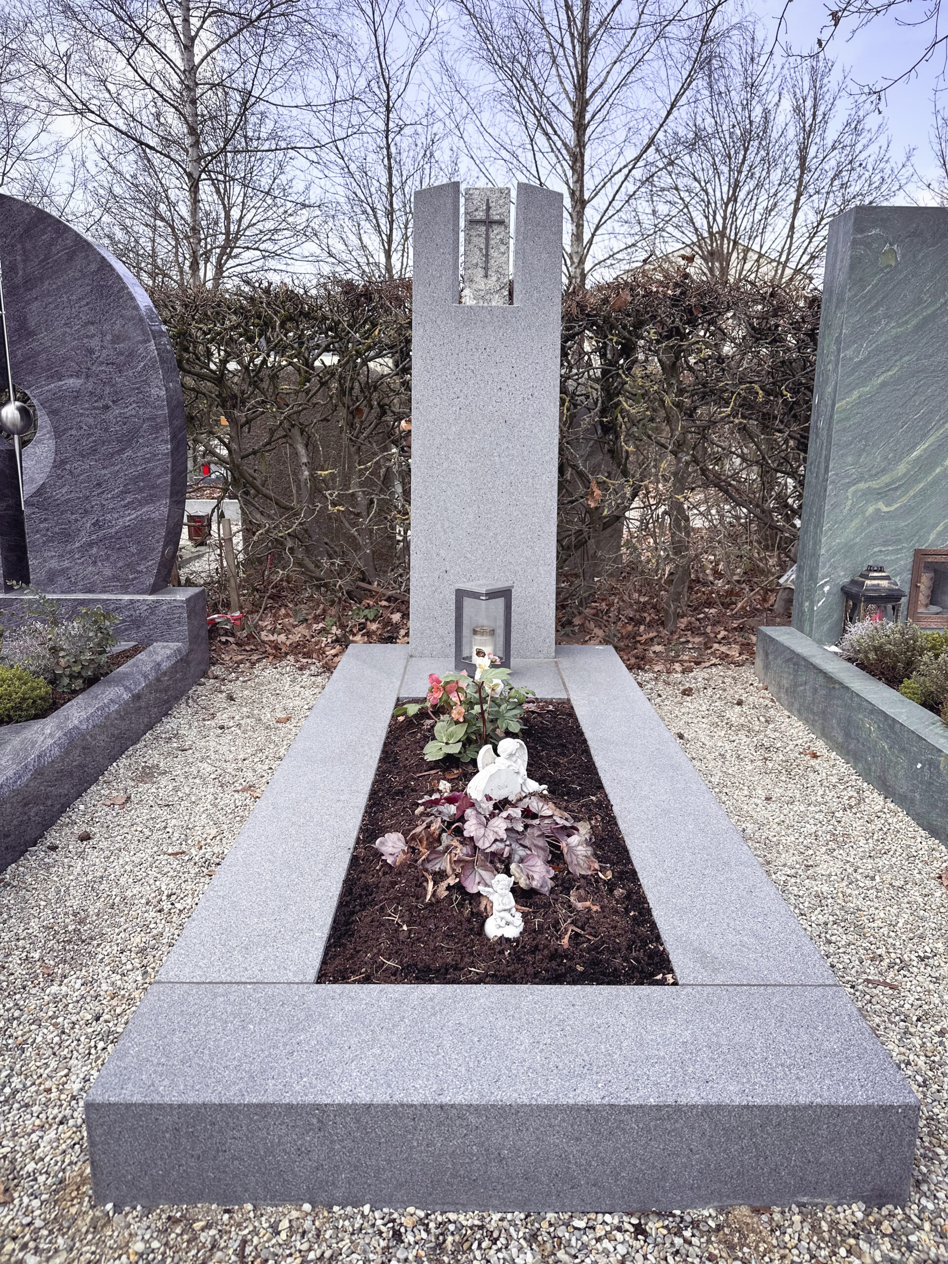 Granit-Grabmal mit kleinem Kreuz und heller Grabfigur