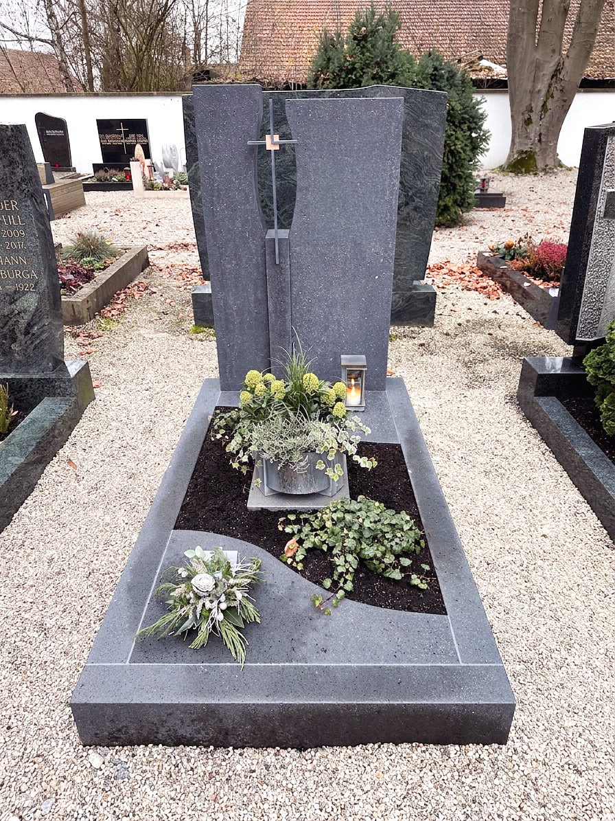 Zweiteiliges dunkles Granit-Grabmal mit Kreuz und winterlicher Bepflanzung