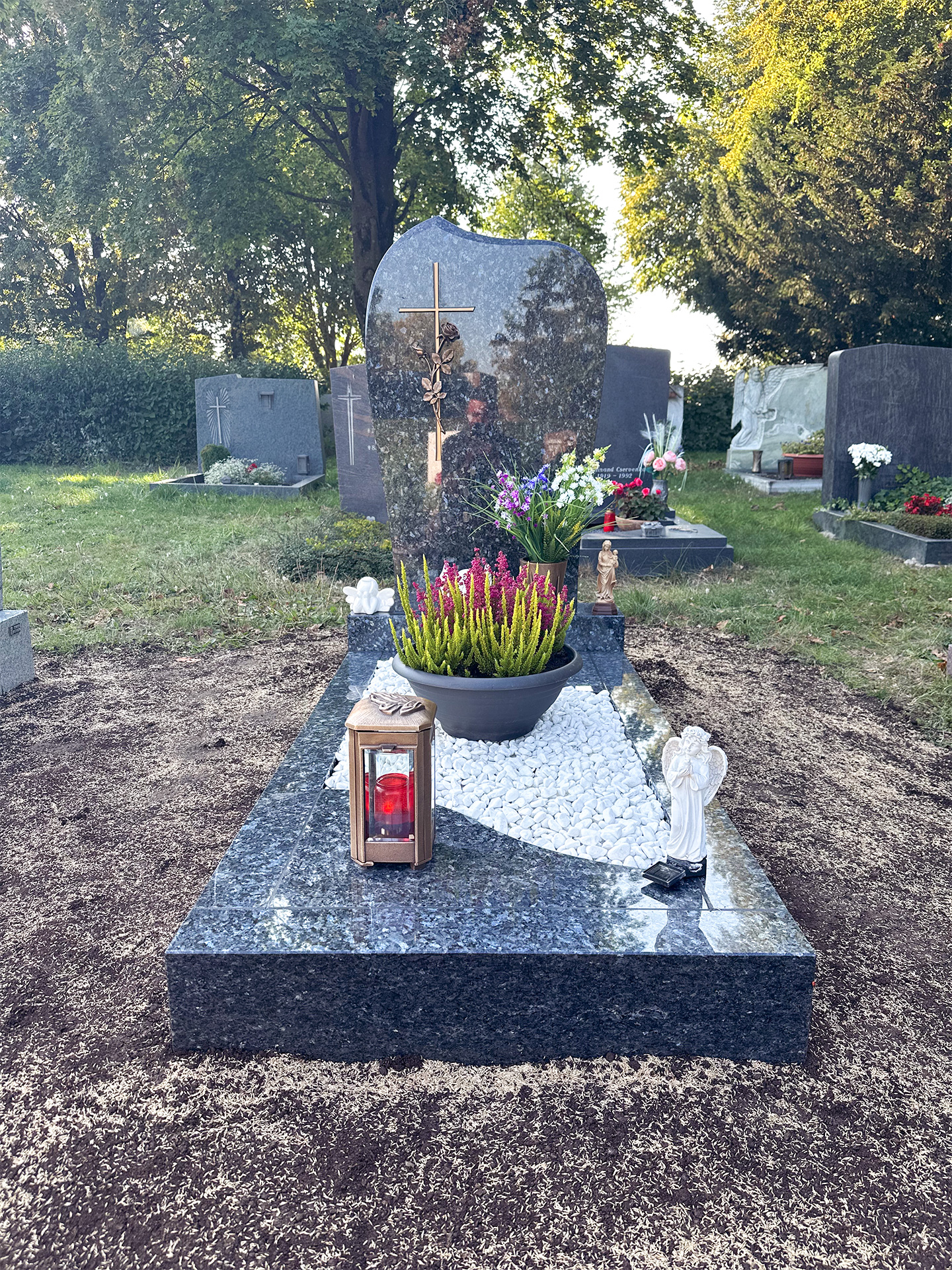 Grabmal aus marmoriertem Granit mit bronzenem Kruzifix und Bepflanzung