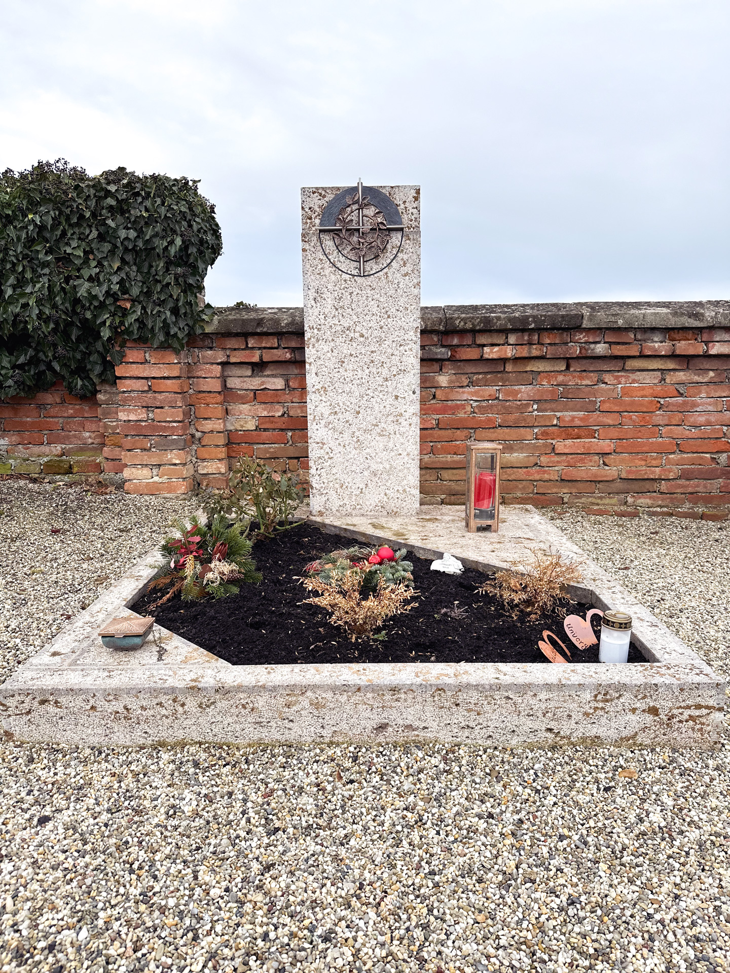 Granit-Grabmal mit bronzenem Medaillon vor einer Friedhofsmauer