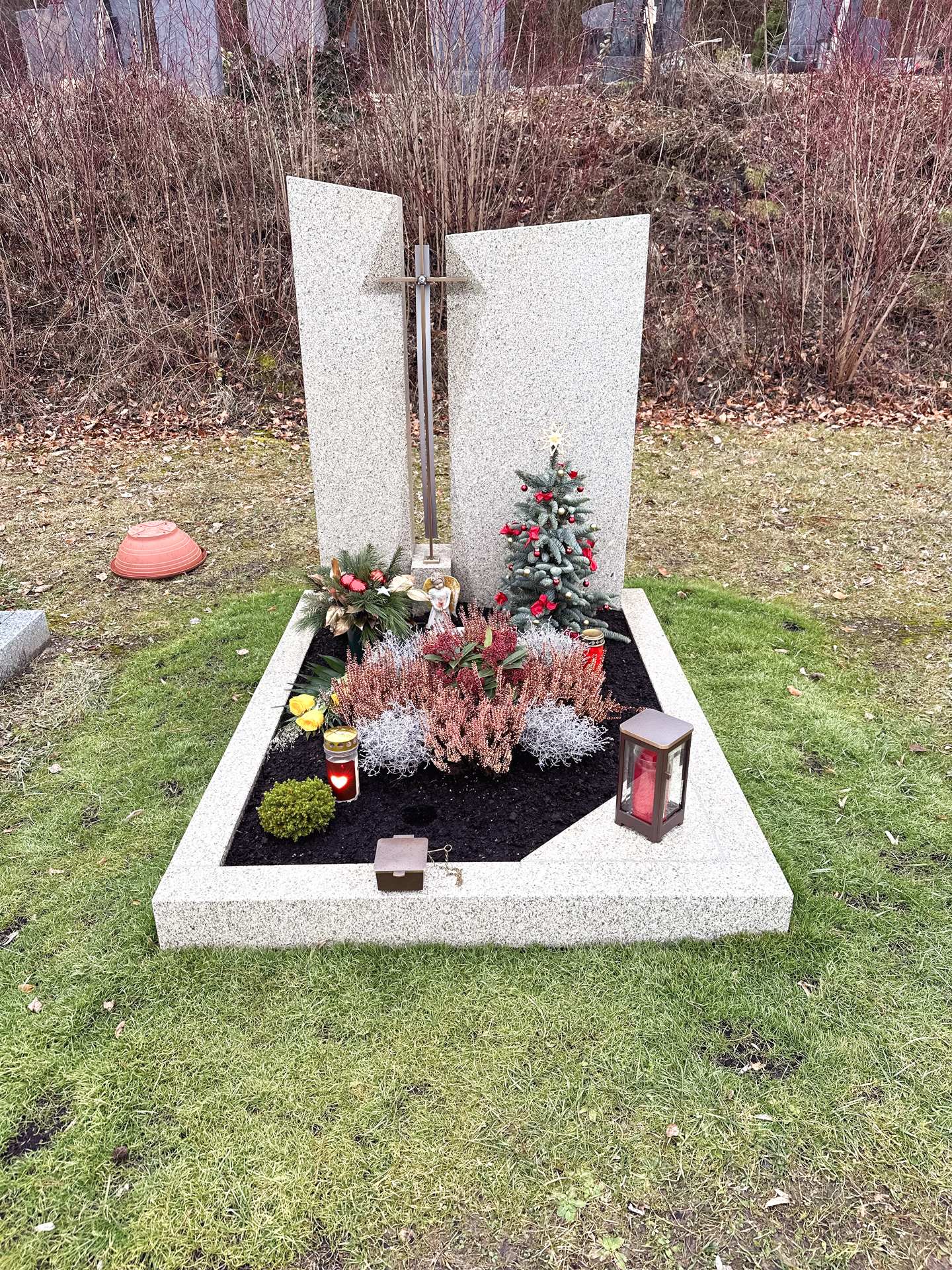 Helles Granit-Grabmal mit Kreuz und weihnachtlicher Grabdekoration