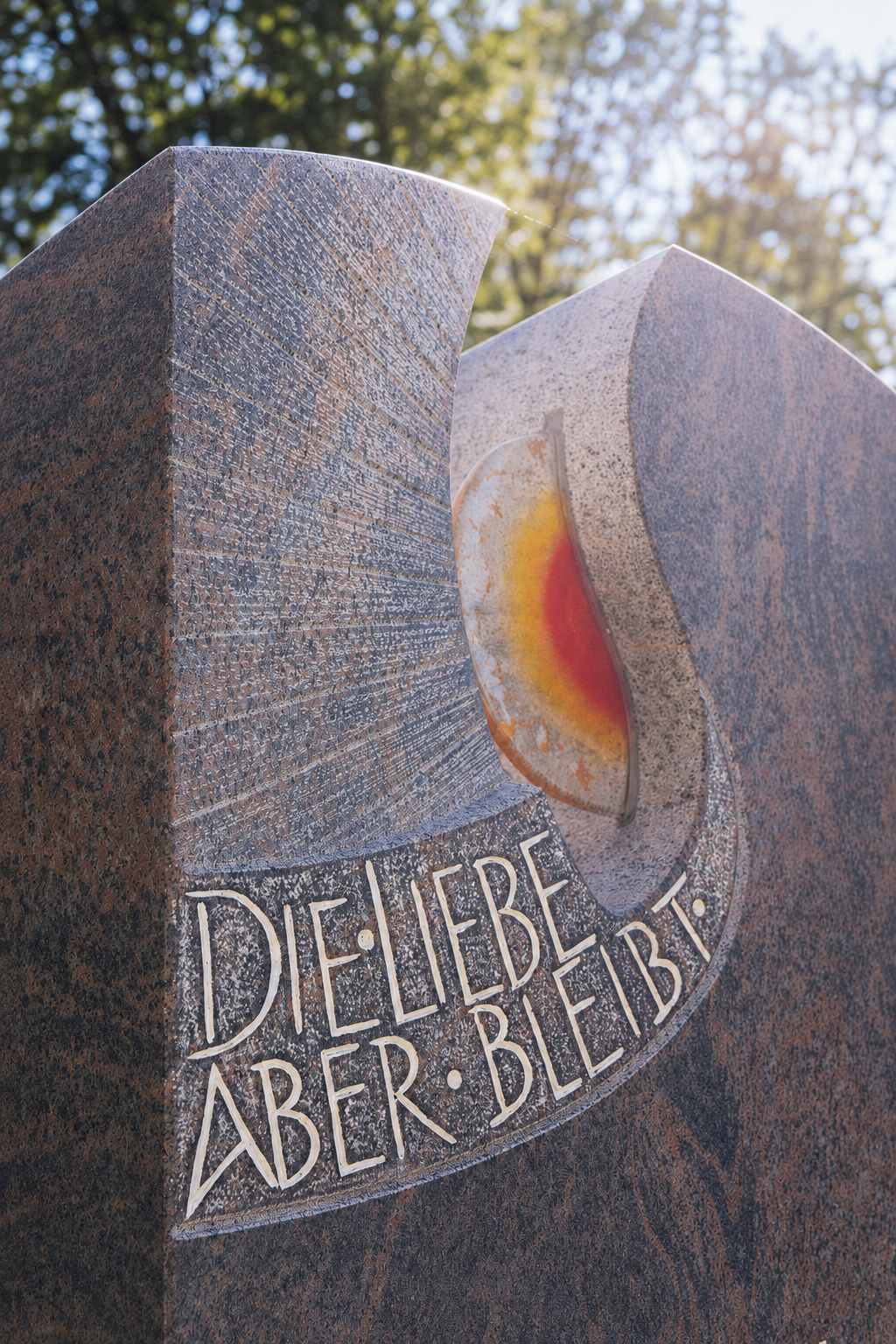Granit-Grabmal mit eingravierter Inschrift „Die Liebe aber bleibt" und farbigem Glasdekor