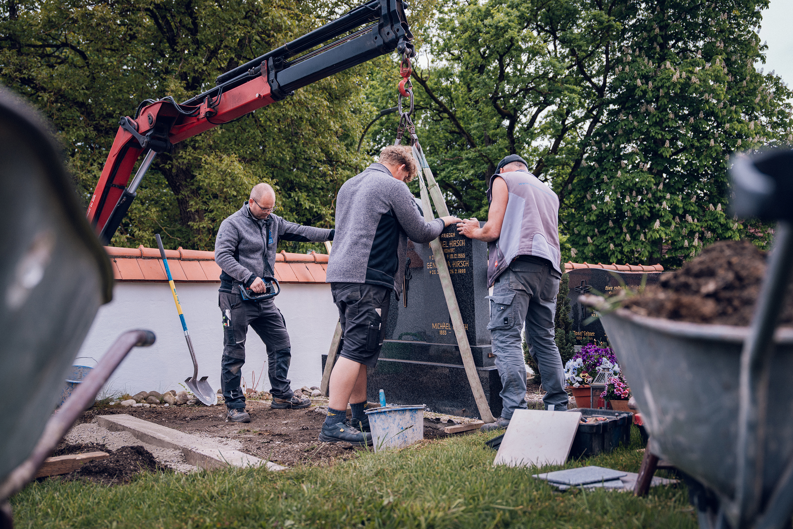 Drei Mitarbeiter setzen mit einem Kran ein Granit-Grabmal auf dem Friedhof