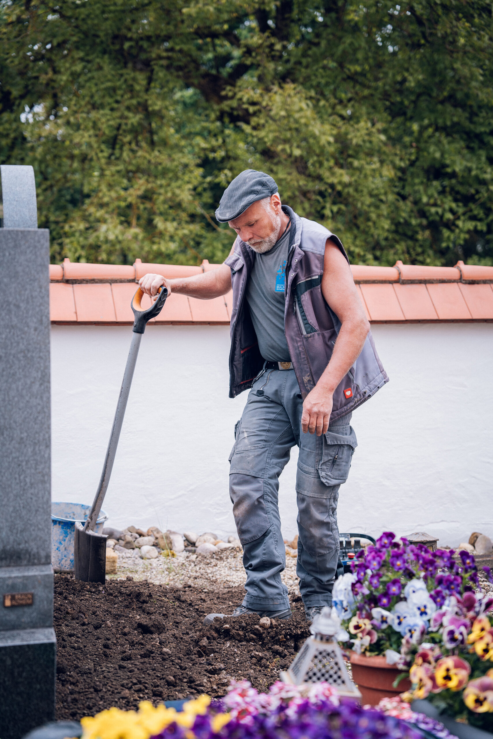Mitarbeiter modelliert mit dem Spaten das Erdreich eines Grabbeetes