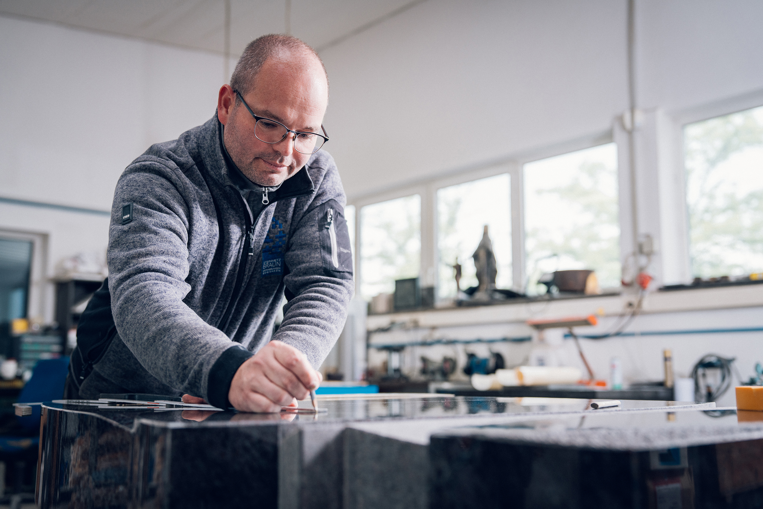 Steinmetz zeichnet ein Motiv auf einem dunklen Granit-Grabstein an