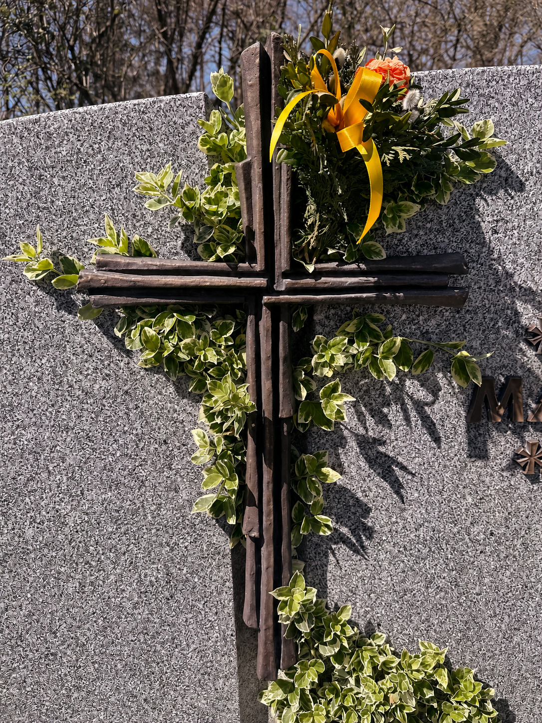 Mit Efeu umranktes Holzkreuz und gelbe Rose auf einem Granit-Grabstein