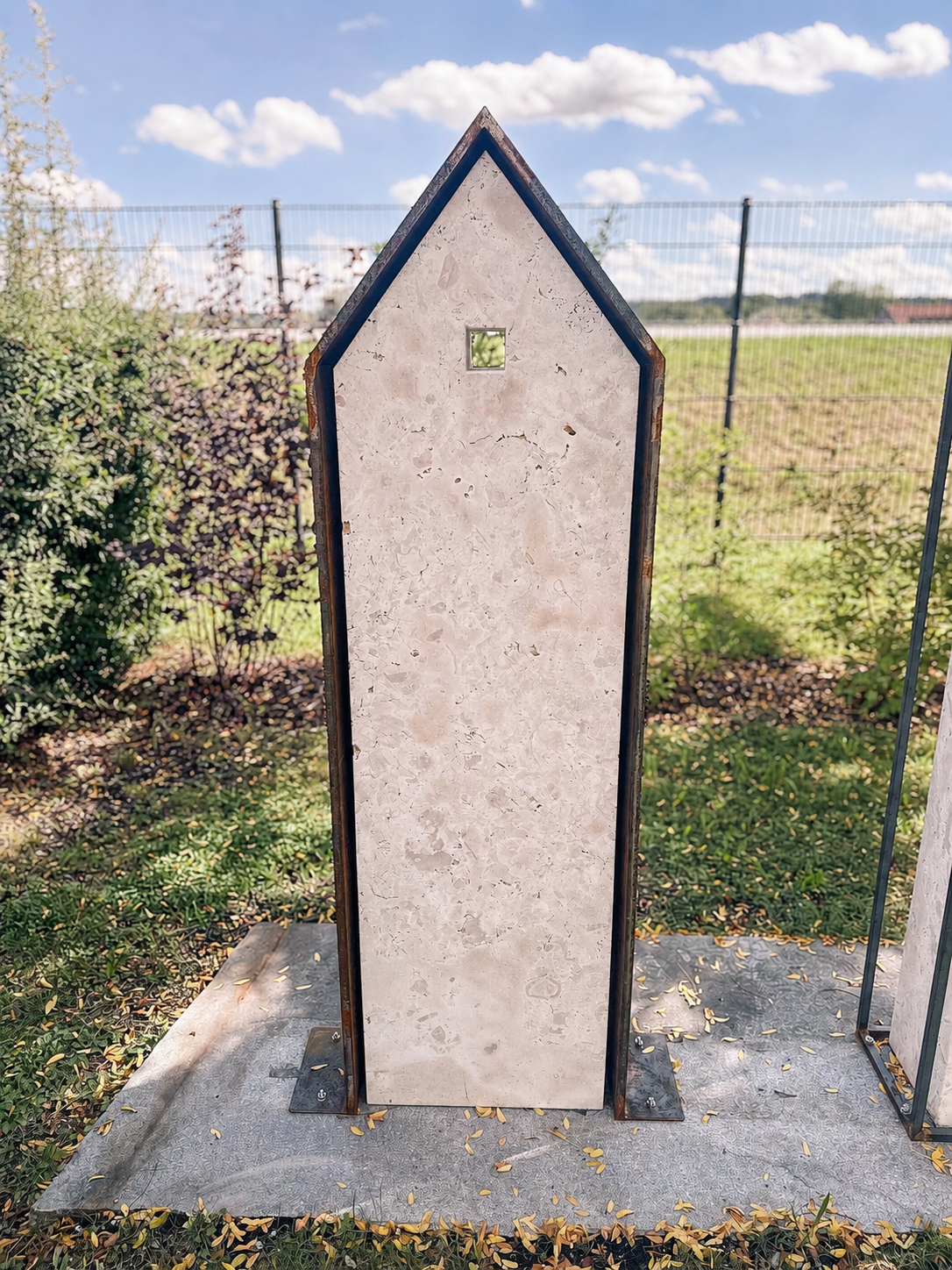 Spitz zulaufende Stele aus hellem Naturstein in einem Metallrahmen