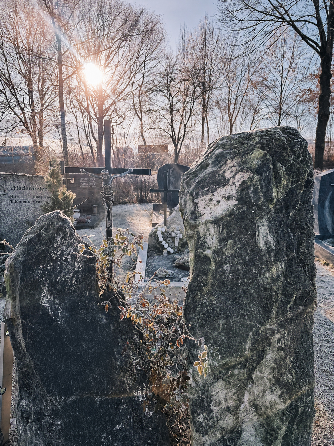 Zwei naturbelassene Findlings-Grabsteine mit Kreuz im winterlichen Gegenlicht