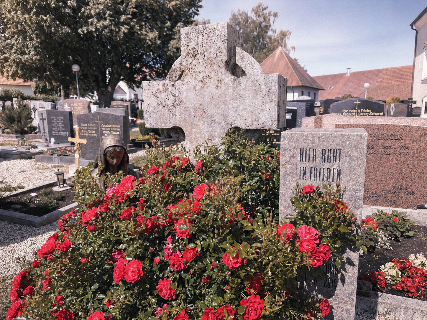 Renoviertes Sandstein-Grabkreuz mit roten Rosen auf dem Friedhof