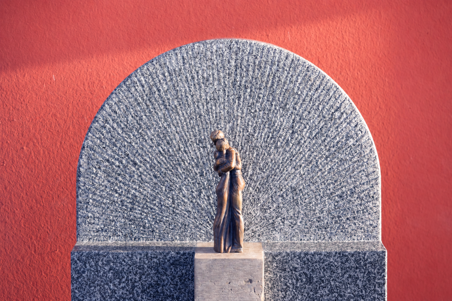 Bronzefigur einer Frau in einer Granit-Nische vor roter Wand