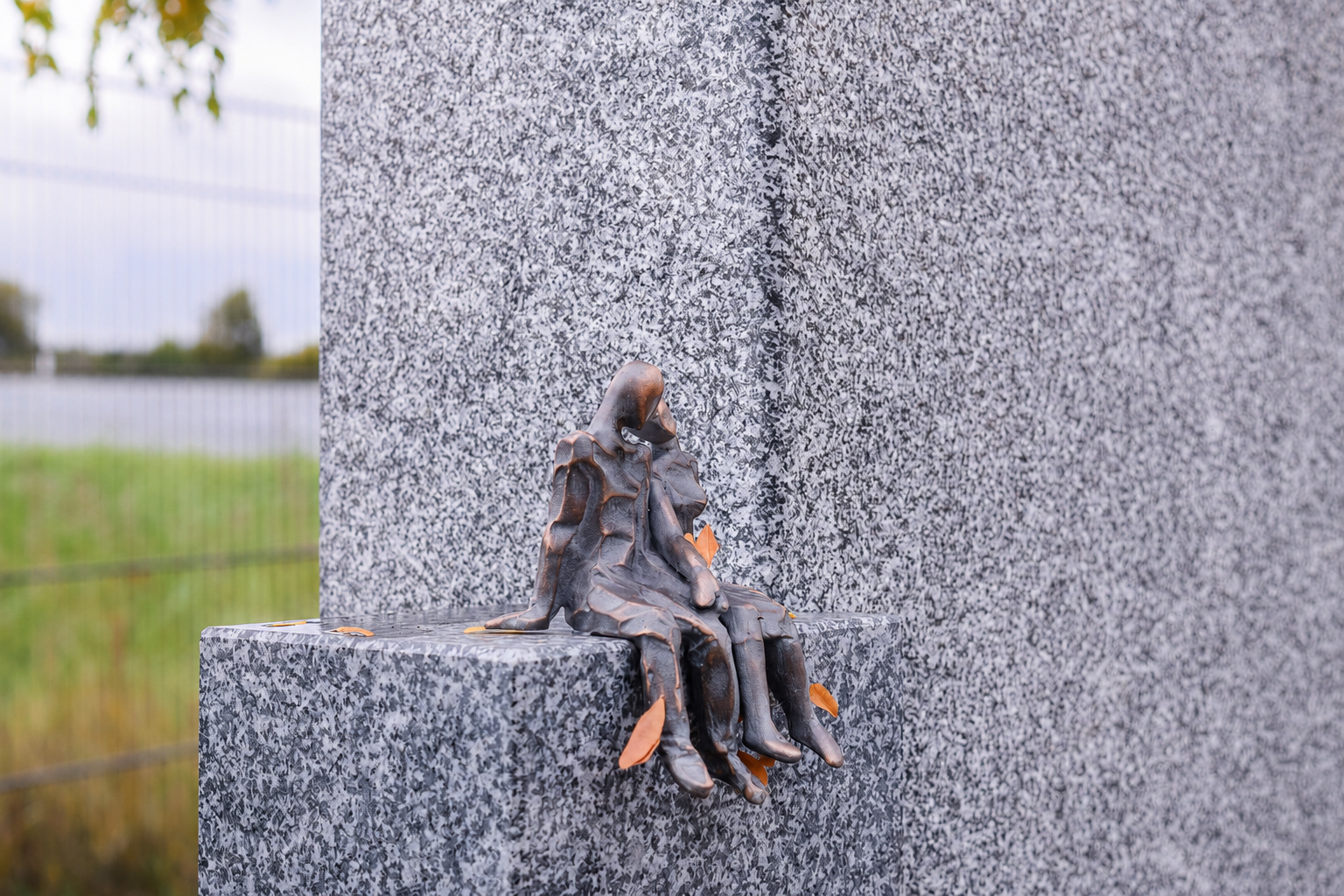 Bronzefigur eines sitzenden Paares am Rand eines Granit-Grabsteins